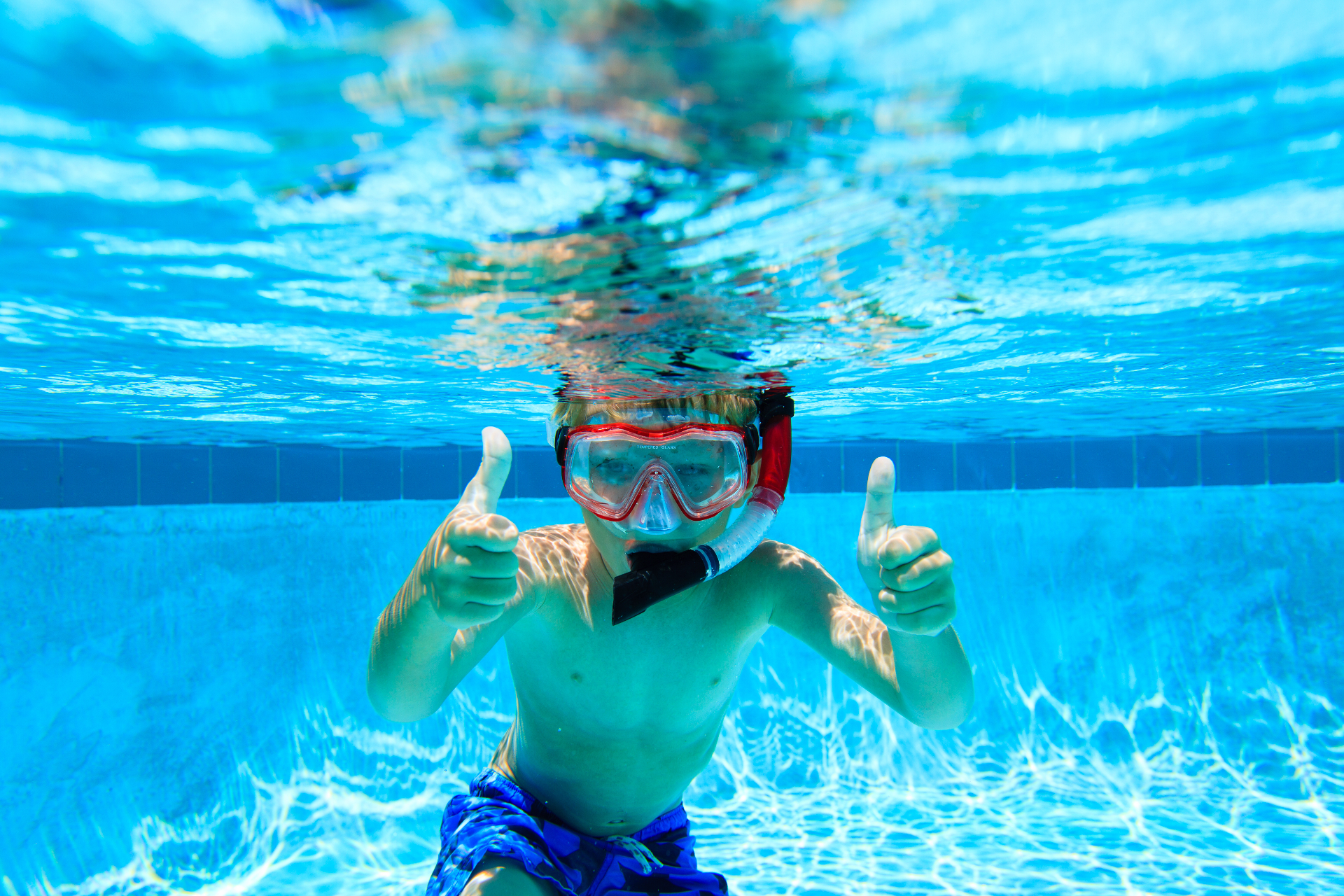 Boy underwater in a pool giving two thumbs up