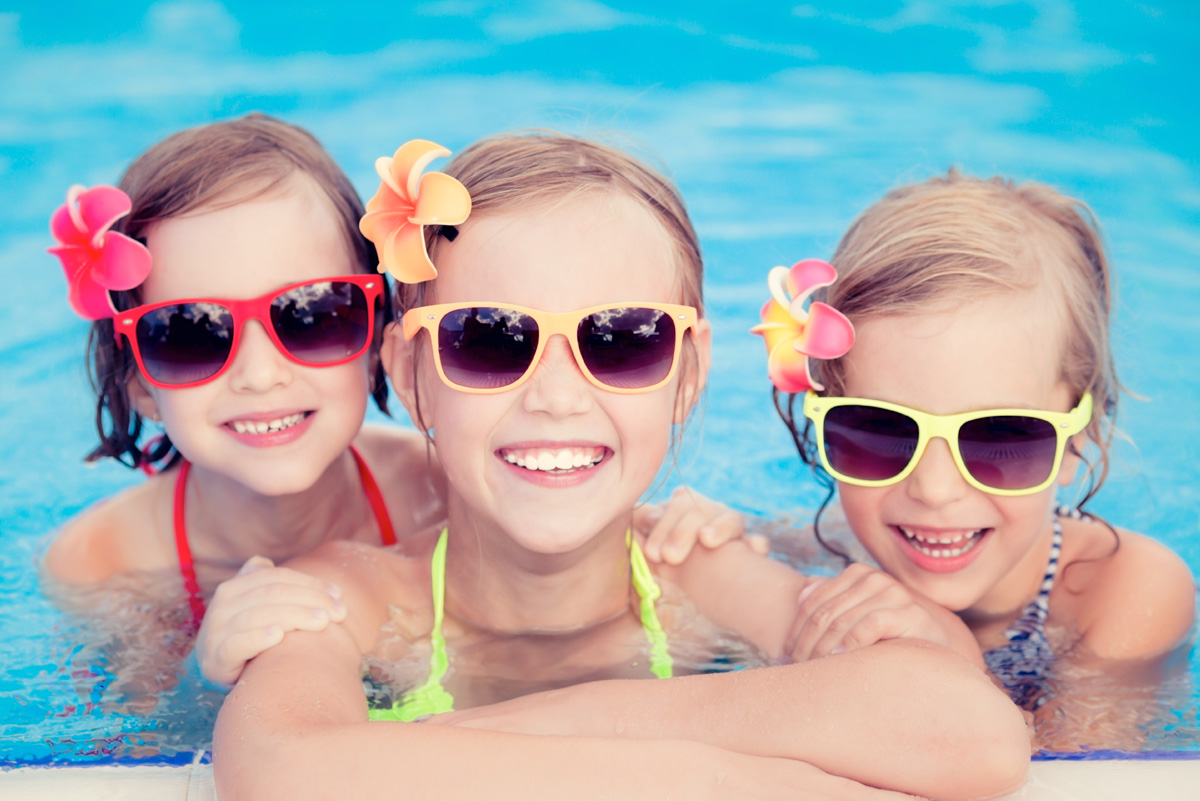 Three happy kids wearing colorful sunglasses in a sparkling clean pool