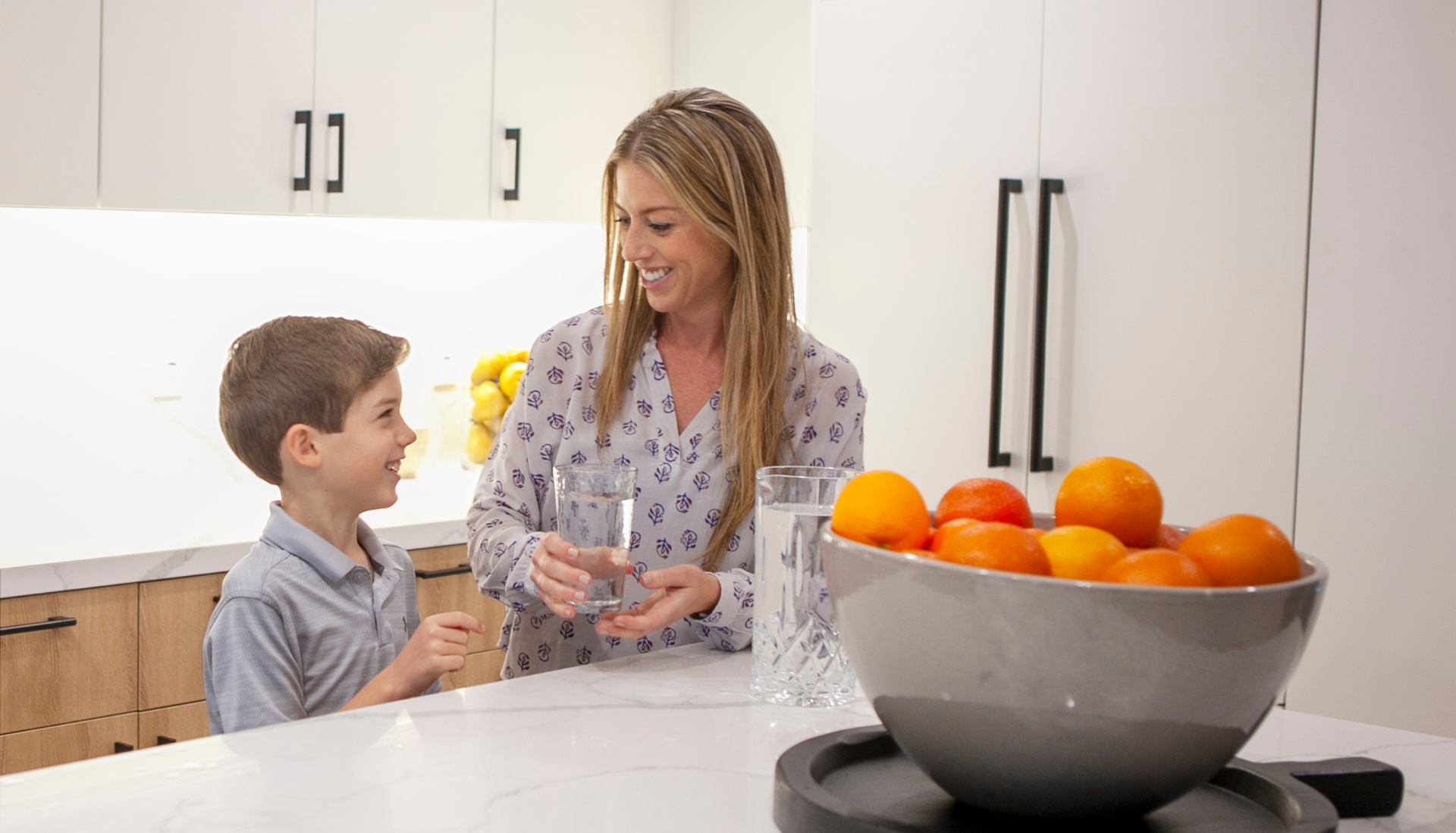 Mom handing her son a glass of clean, soft water in a modern kitchen