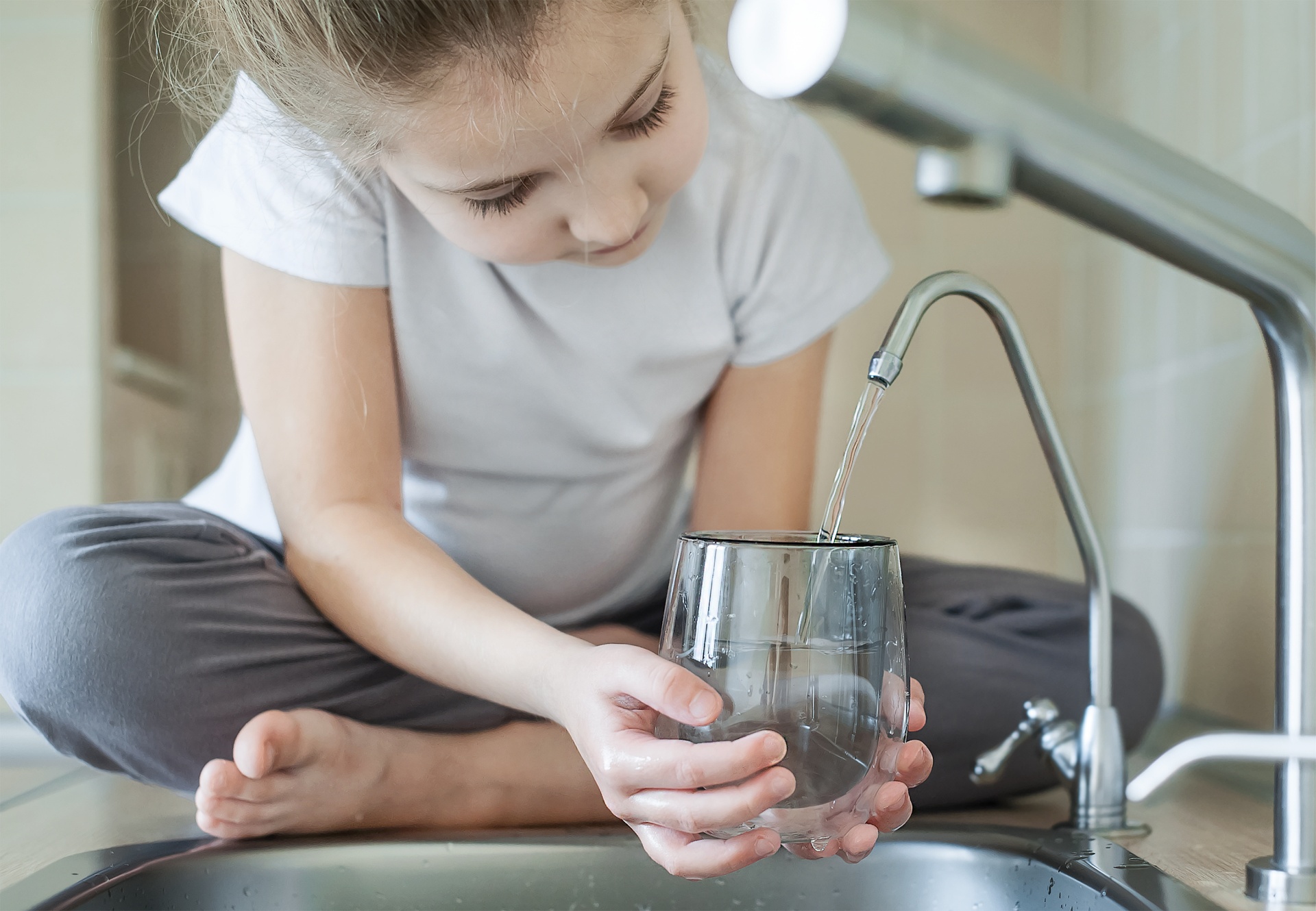 Young girl filling a glass with clean water from a reverse osmosis drinking faucet