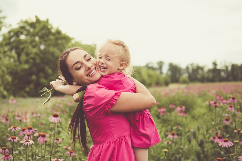 Mother and daughter in pink embracing in a field of pink flowers