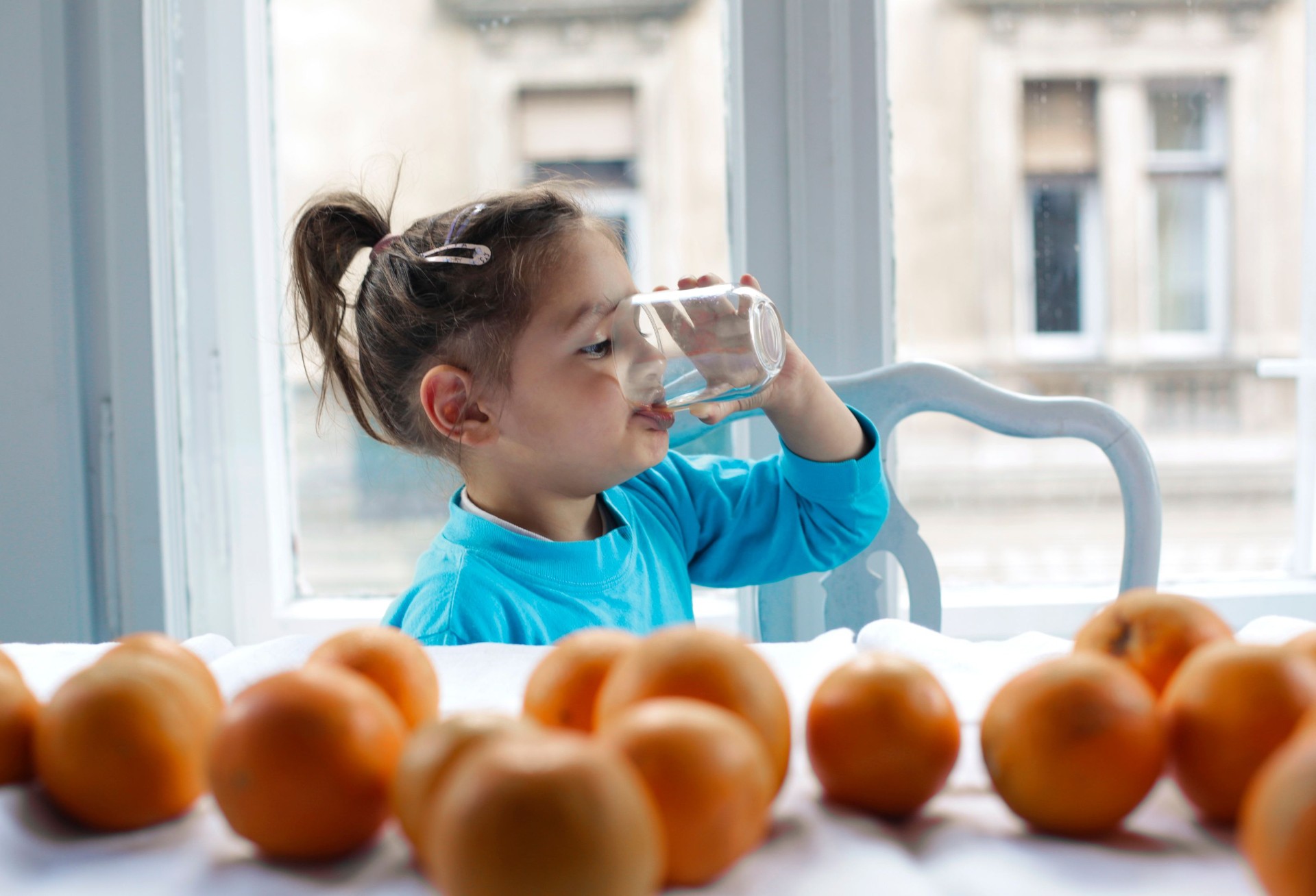 Young girl drinking a glass of clean water at a sunny window